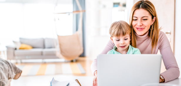 Eine lächelnde Frau schaut im Homeoffice zusammen mit einem Kind auf einen Laptop.